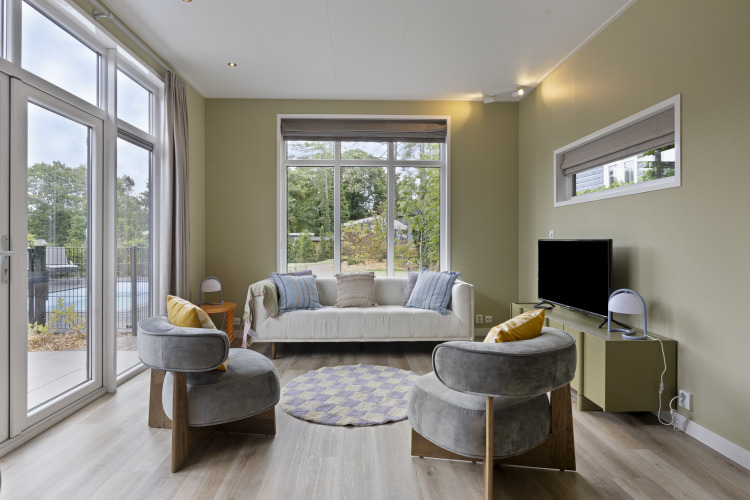 Helles Wohnzimmer einer Lodge mit großen Fenstern, modernen Sesseln und Blick ins Grüne in De Thijmse Berg.