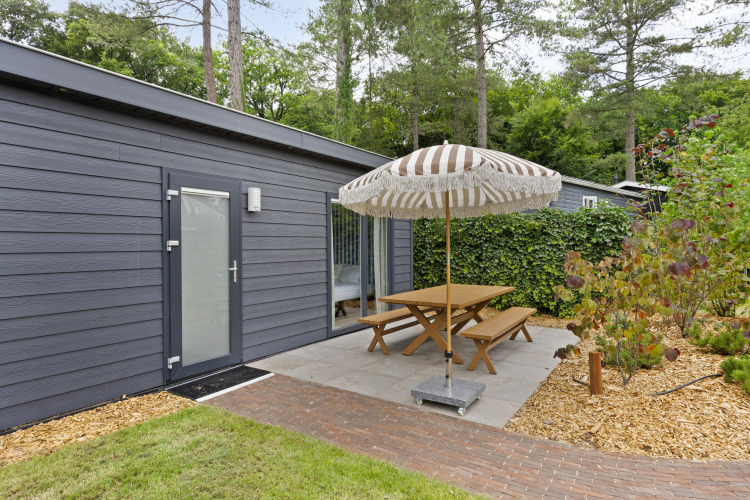 Gemütlicher Außenbereich mit Picknicktisch und Sonnenschirm an einer modernen Lodge in De Thijmse Berg, Niederlande.