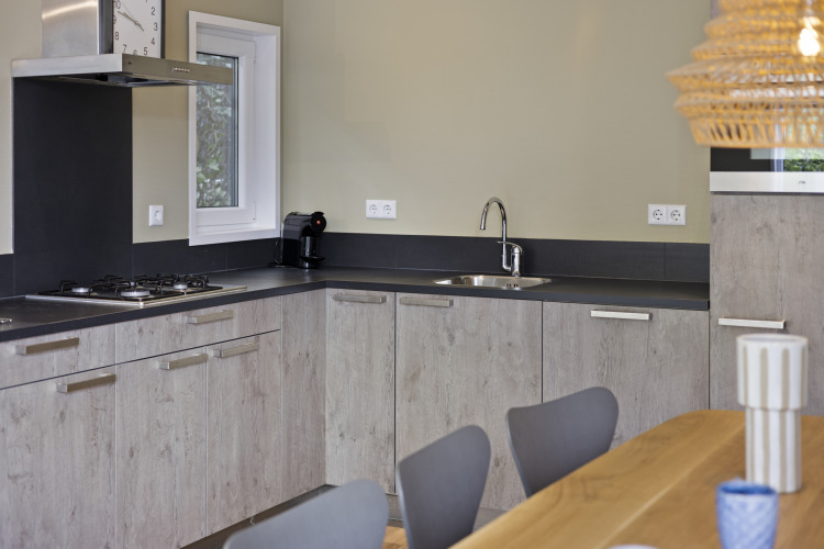 Moderne Eckküche mit hellem Holz, Gasherd, Spüle, Kaffeemaschine und Esstisch in einer niederländischen Lodge.