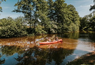 Twee mensen kajakken op een rustige rivier omgeven door groene bomen in Beerze Bulten, Overijssel.
