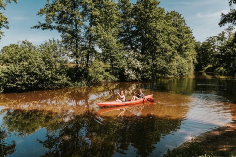 Twee mensen kajakken op een rustige rivier omgeven door groene bomen in Beerze Bulten, Overijssel.