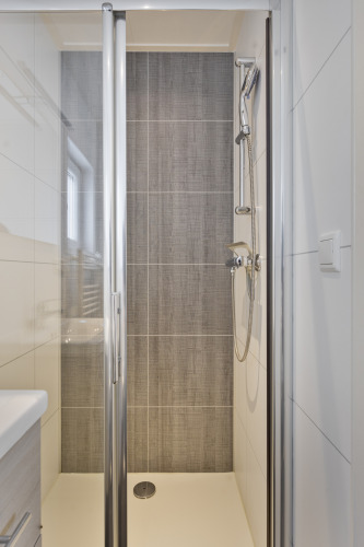 Moderne, schmale Duschkabine mit Glastür und grauen Fliesen, aufgenommen in einer Lodge in den Niederlanden.