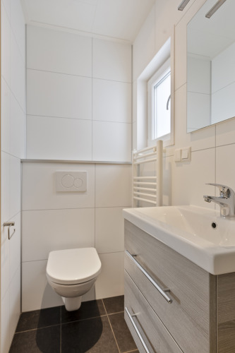 Modernes Badezimmer mit Wandtoilette, Waschbecken, Spiegel und Fenster in einer Lodge am De Thijmse Berg, Niederlande.