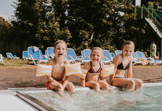 Drie lachende kinderen met zwembandjes zitten aan de rand van het zwembad bij Beerze Bulten, Overijssel.