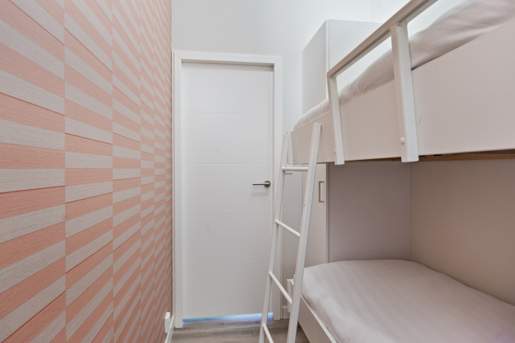 Schmales Schlafzimmer mit Etagenbett, weißer Tür und gestreifter Wand in der 10-Personen-Lodge De Thijmse Berg, Niederlande.