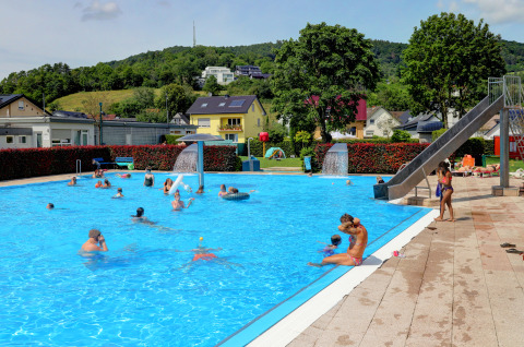 Des personnes se baignent à la piscine du Campingpark Echternacherbrück, entourée de collines verdoyantes en Allemagne.