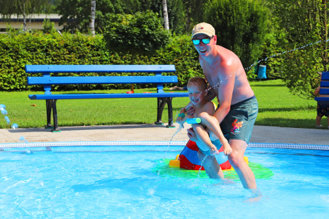 Ein Mann und ein Kind spielen fröhlich im Pool im Campingpark Echternacherbrück in Rheinland-Pfalz.