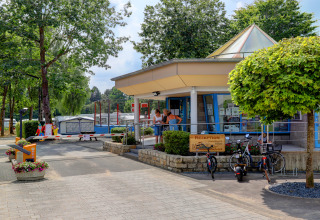 Reception del Campingpark Echternacherbrück in Germania, con biciclette, alberi e roulotte vicine.