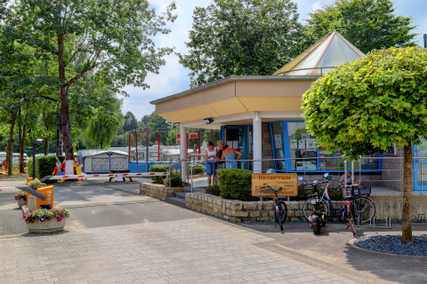 Receptie van Campingpark Echternacherbrück in Duitsland, omringd door fietsen, bomen en caravans.