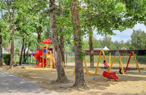 Playground with swings, slide, and trees at Campingpark Echternacherbrück in Rhineland-Palatinate, Germany.