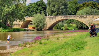 Steinbrücke über einen Fluss mit Menschen und Hund im Urlaubspark Campingpark Echternacherbrück, Deutschland.