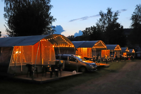 Tende da campeggio illuminate e auto al tramonto al Campingpark Echternacherbrück, Renania-Palatinato, Germania.