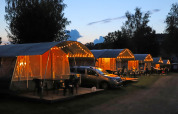 Tende da campeggio illuminate e auto al tramonto al Campingpark Echternacherbrück, Renania-Palatinato, Germania.