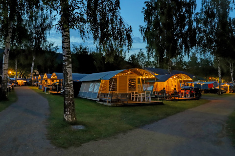 Evening view at Campingpark Echternacherbrück, Germany, showing lit cabins and a relaxing atmosphere.