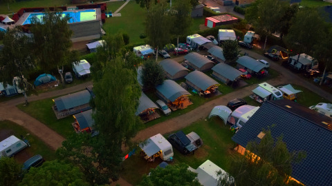 Vista aerea del Campingpark Echternacherbrück in Germania con roulotte, tende e piscina illuminata di sera.