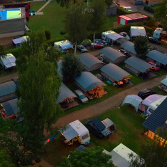Luftaufnahme des Campingpark Echternacherbrück in Rheinland-Pfalz mit Wohnwagen, Zelten und beleuchtetem Pool am Abend.