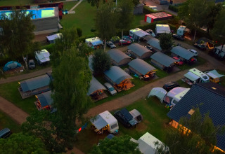 Luchtbeeld van Campingpark Echternacherbrück in Duitsland met caravans, tenten en een verlicht zwembad 's avonds.