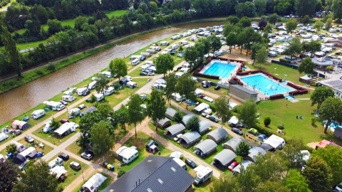 Aerial view of Campingpark Echternacherbrück in Germany with tents, caravans, pools, and a river.