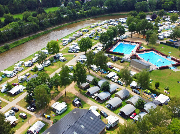 Luchtfoto van Campingpark Echternacherbrück in Duitsland met tenten, caravans, zwembaden en een rivier.