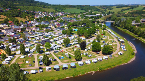 Luchtfoto van de camping in Echternacherbrück, Duitsland, met campers langs een rivier en veel groen.