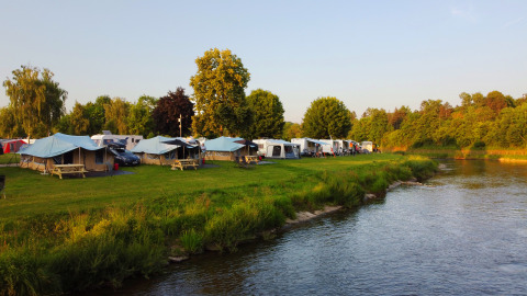 Campingpark Echternacherbrück set fra flodbredden med telte, campingvogne og grønne omgivelser i Tyskland.