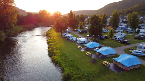 Campingpark Echternacherbrück in Rhineland-Palatinate, Germany, with tents and caravans by a river.