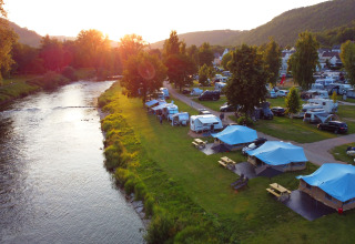 Campingpark Echternacherbrück in Rhineland-Palatinate, Germany, with tents and caravans by a river.