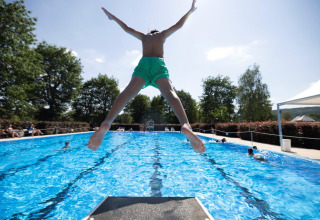 Bambino salta dal trampolino nella piscina del Campingpark Echternacherbrück, Renania-Palatinato, Germania.