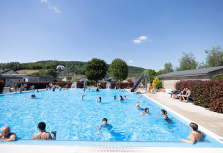 Outdoor swimming pool with guests, sunny weather and green hills at Campingpark Echternacherbrück, Germany.