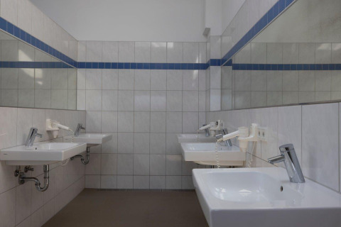 Communal bathroom with white sinks, mirrors, and hairdryers at Campingpark Echternacherbrück in Germany.