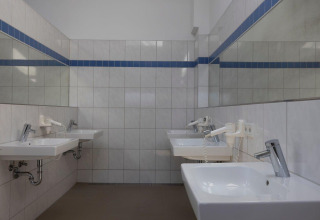 Salle de bains commune avec lavabos blancs, miroirs et sèche-cheveux au Campingpark Echternacherbrück en Allemagne.