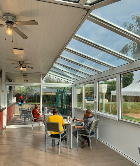 Persone sedute ai tavoli in una luminosa veranda di vetro al Campingpark Echternacherbrück, Renania-Palatinato, Germania.