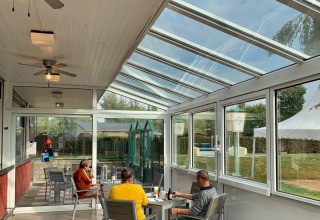 Persone sedute ai tavoli in una luminosa veranda di vetro al Campingpark Echternacherbrück, Renania-Palatinato, Germania.