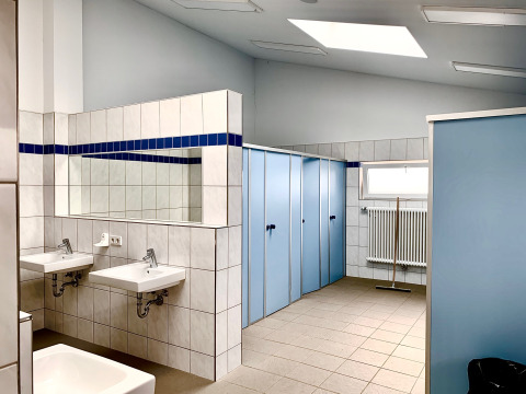 Clean, modern communal bathroom with blue stalls, sinks, and a mirror at Campingpark Echternacherbrück.