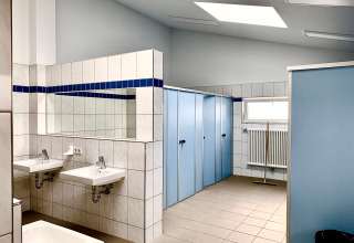 Clean, modern communal bathroom with blue stalls, sinks, and a mirror at Campingpark Echternacherbrück.