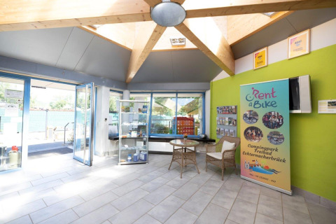Bright reception area at Campingpark Echternacherbrück with Rent a Bike banner, glass walls, and seating.