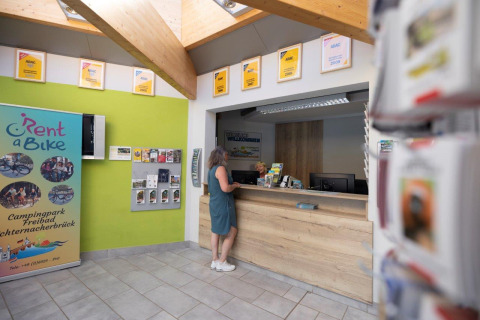 Receptionen på Campingpark Echternacherbrück i Tyskland med en gæst ved skranken og informationsmateriale.