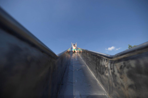 Child seen from the bottom of a slide under a blue sky at Campingpark Echternacherbrück, Germany.
