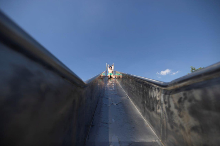 Niño visto desde la base de un tobogán bajo un cielo azul en Campingpark Echternacherbrück, Alemania.