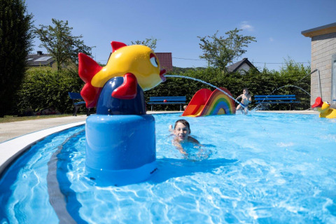 Bambini che giocano in piscina con scivolo e decorazioni colorate al Campingpark Echternacherbrück, Germania.