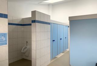 Bagno luminoso e pulito al Campingpark Echternacherbrück con porte azzurre e un solo orinatoio.