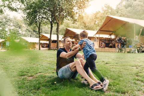 Vader en zoon spelen samen op het grasveld voor safaritenten bij Beerze Bulten vakantiepark in Overijssel.
