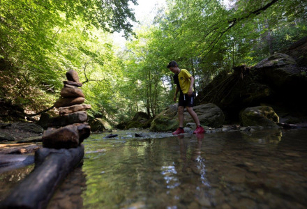 Jongen steekt een ondiepe beek over in de buurt van Echternacherbrück, Duitsland, met een stapel stenen op de voorgrond.
