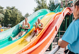 Vaders met kinderen glijden lachend van een kleurrijke waterglijbaan in Beerze Bulten, Overijssel.