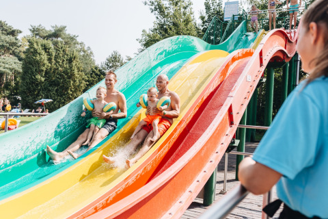 Vaders met kinderen glijden lachend van een kleurrijke waterglijbaan in Beerze Bulten, Overijssel.