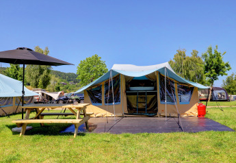 Campsite at Eifel - Echternacherbrück Lodge River with tent, picnic table, umbrella and green nature.