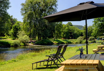 Picnic table and loungers under umbrella by riverside at green park in Campingpark Echternacherbrück, Germany.