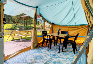 Binnenzicht van lodge tent met tafel en stoelen, picknickbank en rivier buiten aan Campingpark Echternacherbrück.
