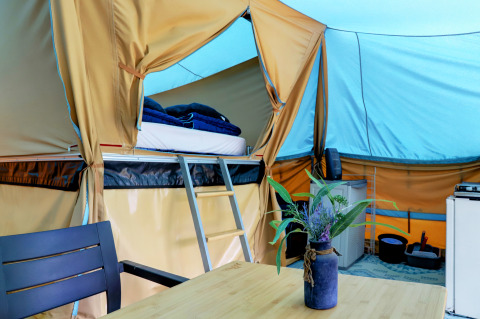 Interieur van een comfortabele lodgetent met stapelbed, tafel, stoelen en bloemenvaas op de camping.