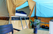 Interieur van een comfortabele lodgetent met stapelbed, tafel, stoelen en bloemenvaas op de camping.